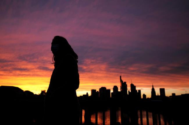 A woman wearing a protective mask walks past the skyline of the financial district during sunset as the spread of the coro<em></em>navirus disease (COVID-19) co<em></em>ntinues in Frankfurt, Germany, October 26, 2020, REUTERS/Kai Pfaffenbach