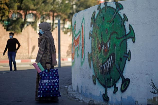 A Palestinian woman wearing on a protective face mask speaks on her phone as she stands next to a coronavirus-themed mural amid the coro<em></em>navirus disease (COVID-19) outbreak, in Gaza City November 22, 2020. REUTERS/Mohammed Salem