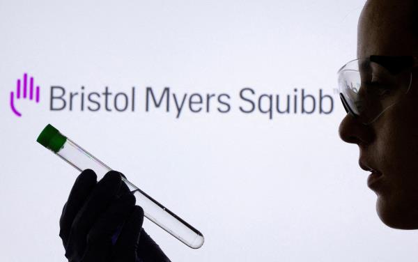 A woman holds test tube in front of displayed Bristol Myers Squibb logo in this illustration