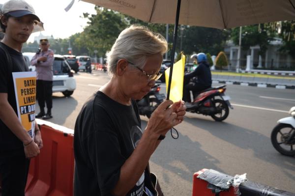 Maria Catarina Sumarsih. The 71-year-old is at a rally outside the Presidential Palace over Indo<em></em>nesian rights abuses. She has white hair and is wearing glasses. She is standing beneath an umbrella. Another protester is beside her.