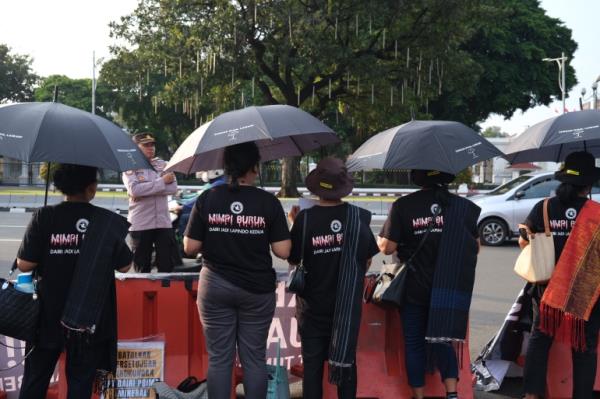 Demo<em></em>nstrators standing beneath black umbrellas. They are on the road opposite the presidential palace in Jakarta. They are wearing T-shirts reading 'dark dreams' on the back