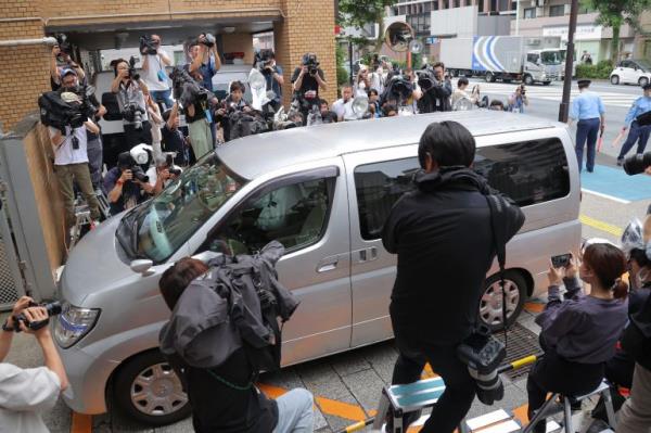 Crowds of reporters and photographers surround a silver coloured vehicle entering a police station in Tokyo. Kabuki actor Ennosuke Ichikawa is inside.