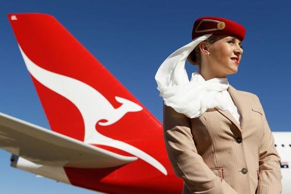 An Emirates Airline flight attendant stands in front of a Qantas Airways aircraft