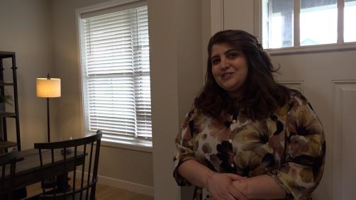 a woman stands in front of a dining room showing off a new model home