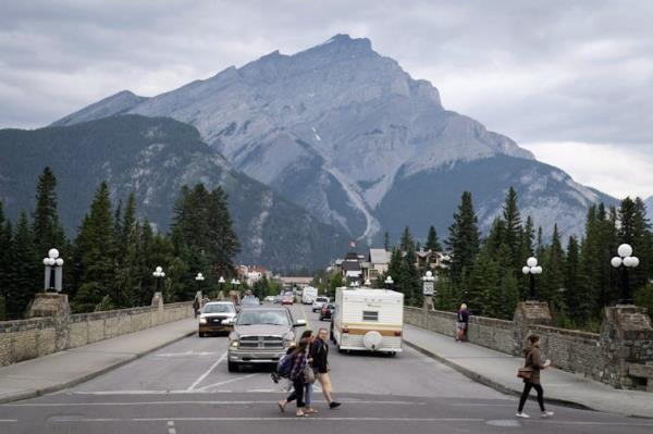 Vehicles on a road, with pedestrians in the foreground and mountains in the background.