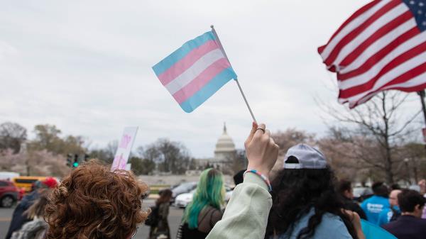 A trans flag is seen as protesters march towards the Capitol