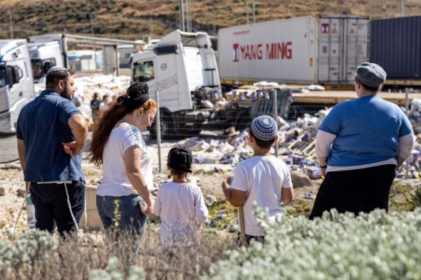 Israeli right-wing activists look at damaged trailer trucks that were carrying humanitarian aid supplies on the Israeli side of the Tarqumiyah crossing with the occupied West Bank on May 13, 2024, after they were vandalised by other activists to protest against aid being sent to the Gaza Strip. (Photo by Oren ZIV / AFP)
