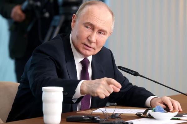 Russian President Vladimir Putin speaks into a microphone at a panel table.