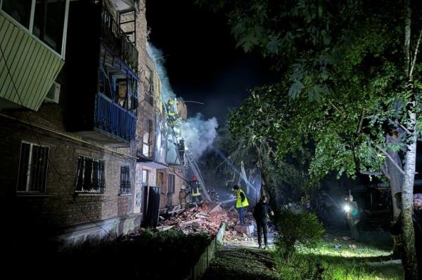 Firefighters at the site of a badly damaged apartment building in Kharkiv after it was hit by a Russian missile. It's night time. The building has been illumintaed. There is a largle pile of rubble, dust and smoke.