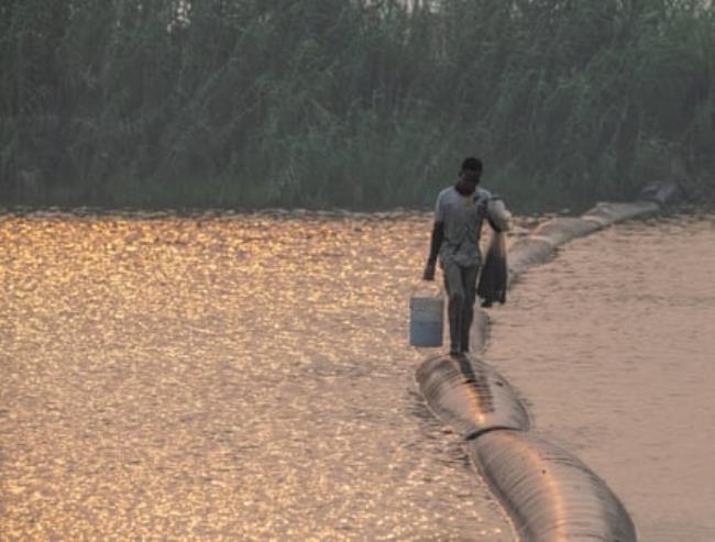 A young boy walking on pipes that cross a river.