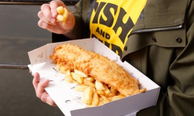 Close up of Daniel’s hands, one holding a packet of fish and chips, the other taking a chip