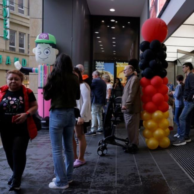 Shoppers shelter from the rain by an entrance to a Dortmund department store that has been decorated with German coloured balloons.