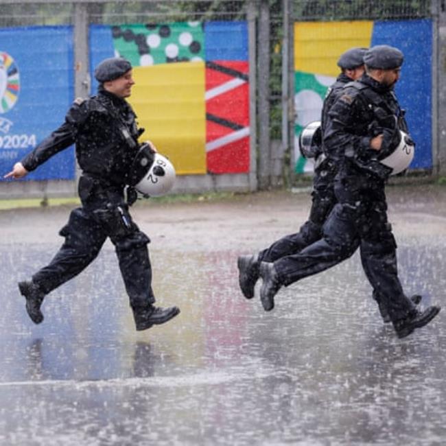 Police run for cover as a thunderstorm hits the ground before the 2024 European Champio<em></em>nship group game between Turkey and Georgia.