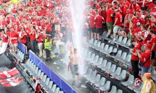 Water piles down on the Denmark fans – one in particular – during the huge storm that halted the match for 25 minutes.