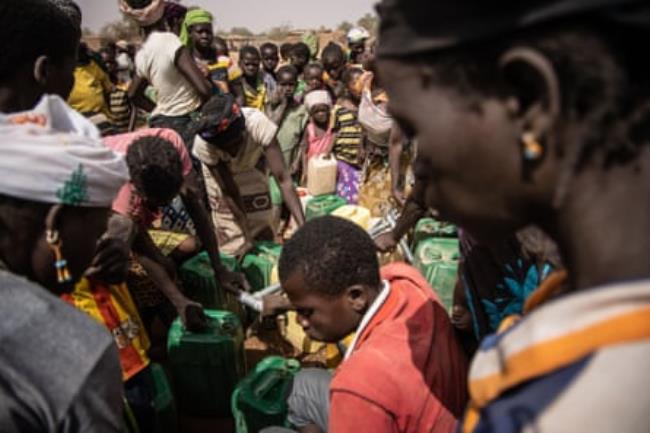 Crowds of people wait in line to collect water from a pump