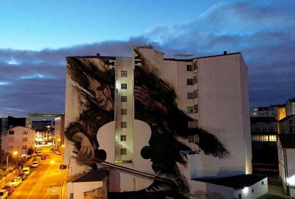 A mural painted by Spanish artist Sfhir depicting a woman that plays the cello, which has been voted the 'Street Art Cities' Best Mural in the World 2023, is seen on two buildings at nightfall, in Fene, northern Spain