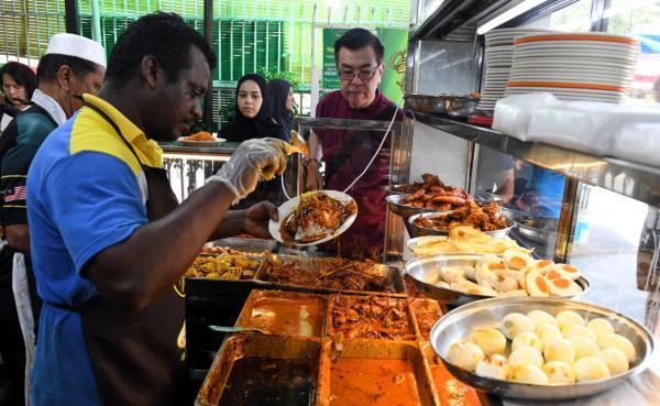 An employee at Restoran Deens Maju Nasi Kandar serves up a hot plate of nasi kandar during peak hours.