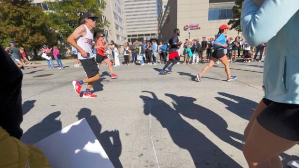 Friends of Jake Rower of Ellicott City cast shadows on Pratt Street as they cheer his effort In the half marathon during the 24th Annual Running Festival at the inner harbor. (Karl Merton Ferron/Staff)