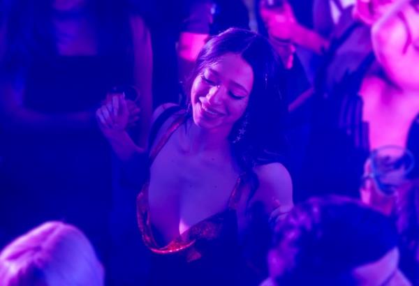 Mikey Madison as Ani in a low-cut red top closes her eyes and dances while bathed in purple light in a nightclub in a scene from Anora