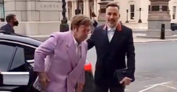 Elton John limping as he steps out of car. David Furnish stands beside him