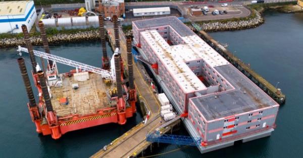 A large multistory rectangular barge moored at a dock.