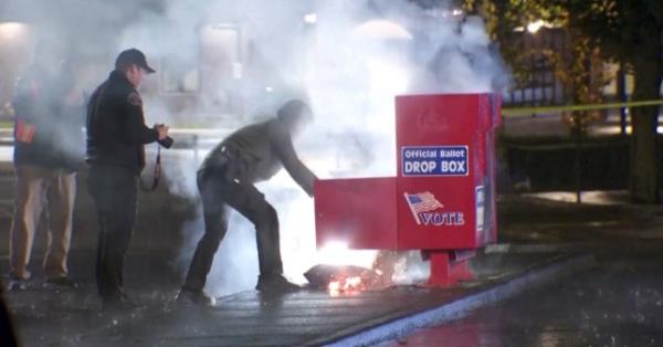 Police officers tend to a smoking ballot drop off box on the street