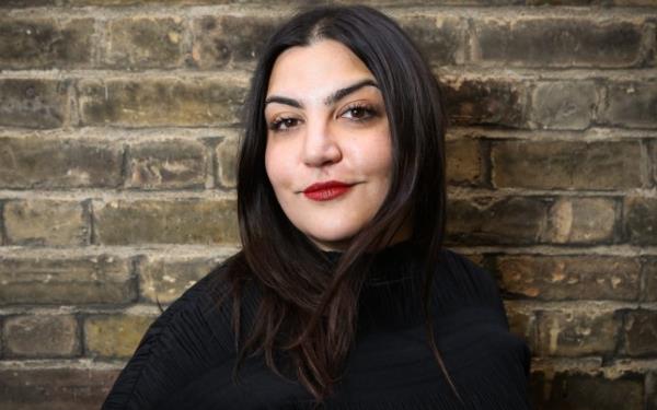 Almara Abgarian wearing red lipstick and a black top standing in front of a brick wall