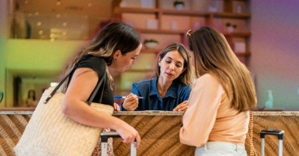 Three women talking at a hotel reception desk with suitcases