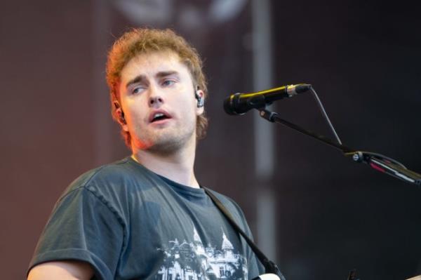 Sam Fender performs on stage, he looks to his left standing next to microphone.