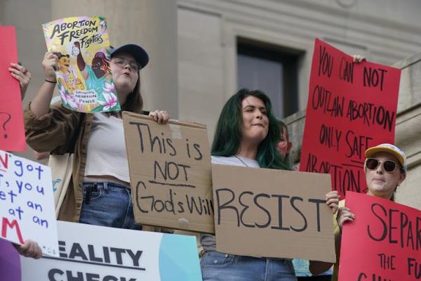 Women protesters carry pro-abortion rights signs, including one that reads 'Resist.'