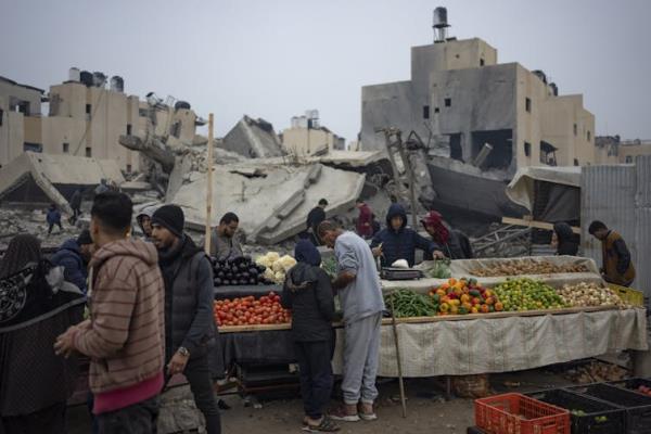 People stand looking over vegetables with rubble in the background.