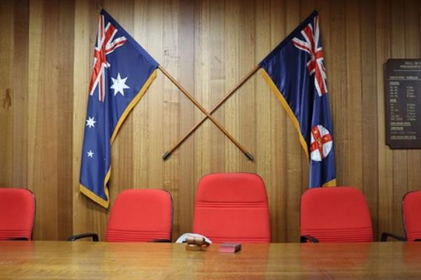 Cooma Council Chambers, head of the meeting table with empty chairs and councillor paraphernalia and state/natio<em></em>nal flags behind.