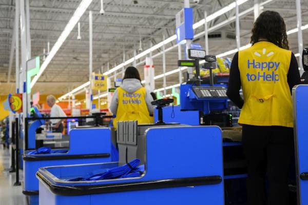 The cashiers, seen from behind, wear yellow vests that say 'Happy to help'