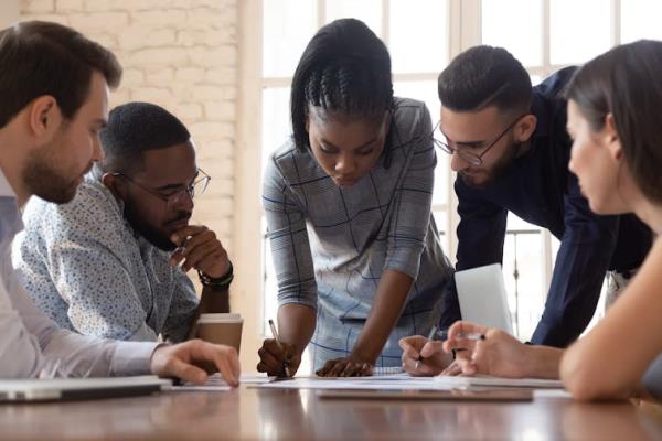 A group of people of diverse racial backgrounds sit around a co<em></em>nference table, looking at a new<em></em>line on it