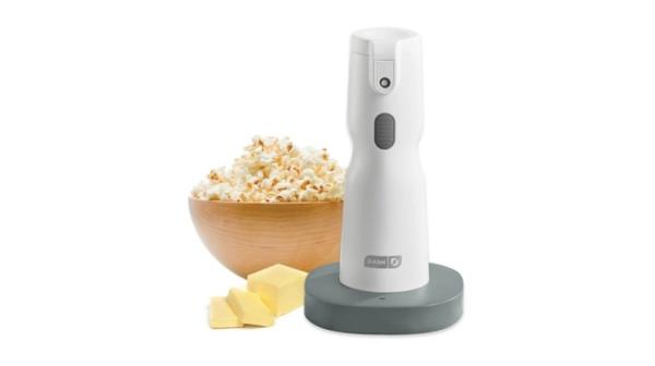 Tall white device with button and nozzle with a bowl of popcorn in the background