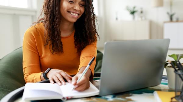 A woman using a laptop while writing on a notebook