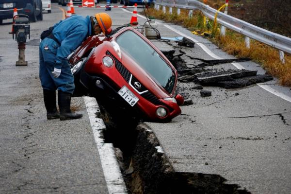 A worker looks at a car stuck on a broken road near Anamizu, Ishikawa Prefecture, on Jan. 3. The Noto Peninsula quake drew attention to the lack of infrastructure co<em></em>nnecting remote communities to possible lifelines. 