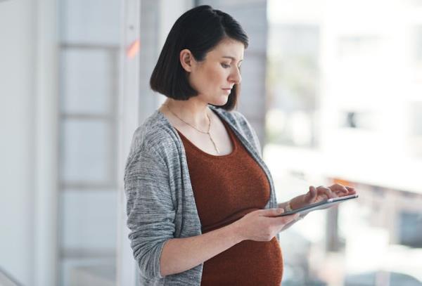 Side profile of a pregnant woman swiping on a tablet