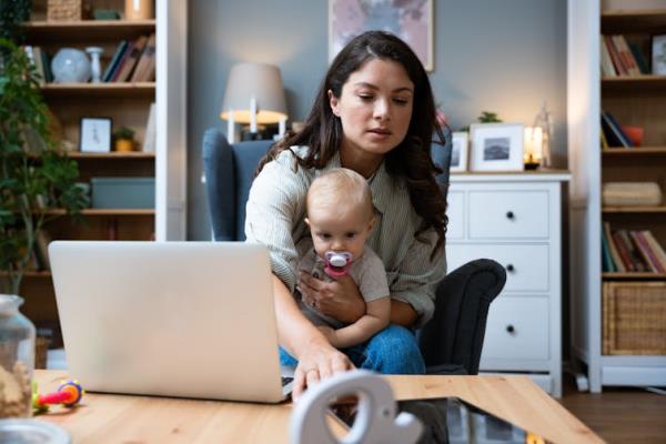 A woman with a toddler in her lap sits in front of an open laptop