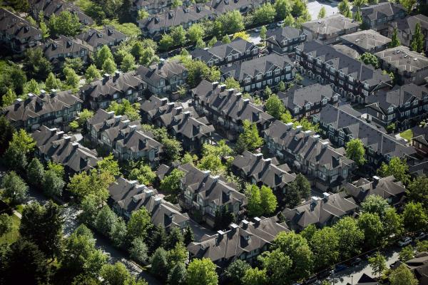 Aerial view of rows of identical townhouses with grey roofs with rows of deciduous trees separating them