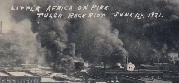 A black-and-white picture showing the Greenwood District in flames during the Tulsa Race Massacre.