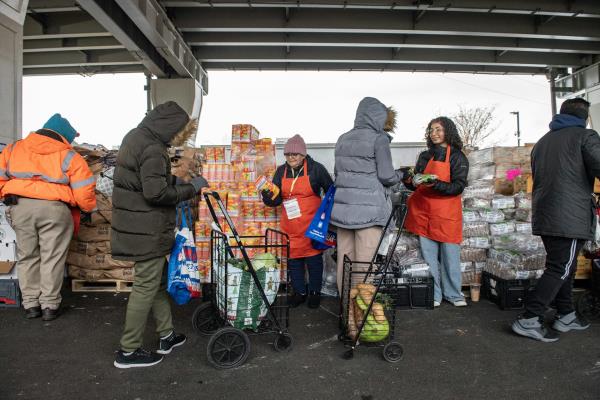 People in orange aprons hand out food outdoors in cold weather to people in parkas.