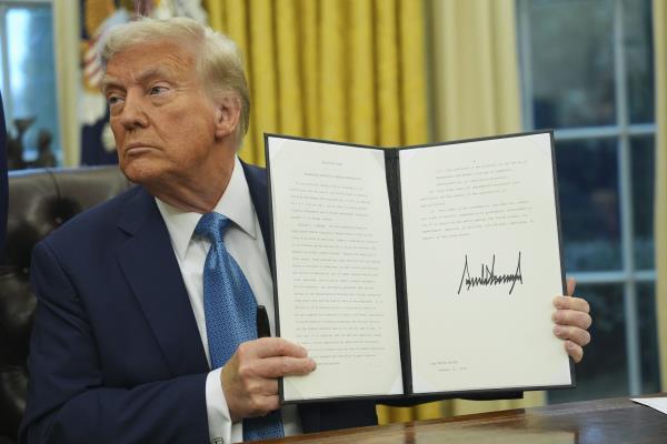 An elderly man with greyish-blond hair holds up a signed new<em></em>line.