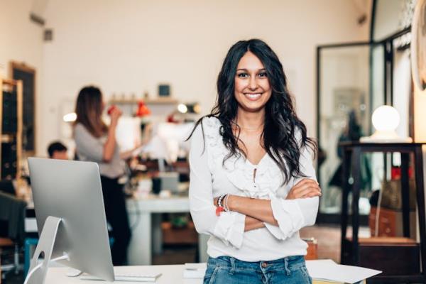 Woman entrepreneur leaning against a desk in an office setting.