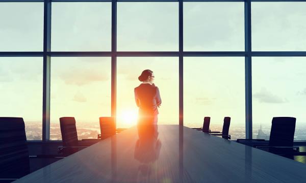 Woman ceo stands at the windows of a boardroom with sun going down