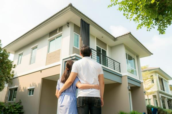 Back portrait of young couple standing and hugging together looking happy in front of their new house