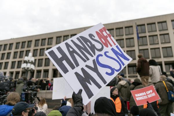 a group of people, some holding signs, stand outside an office building