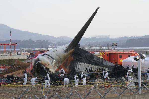 Rescue workers wearing white safety gear work through the wreckage of a burnt plane, which has crashed into the runway at a South Korean airport.