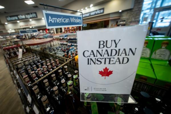 A sign in a liquor store that reads "Buy Canadian Instead". It has been placed in front of bottles of American whiskey.